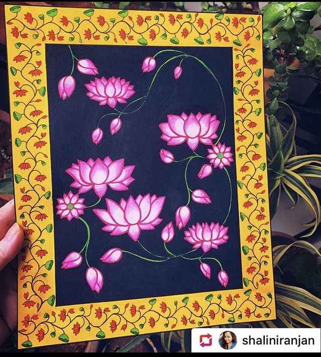 a person holding up a painting with pink flowers on black paper in front of some potted plants