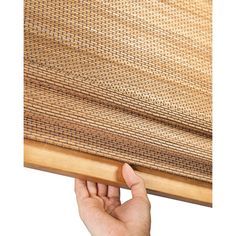 a hand is holding up the edge of a bamboo window covering that's partially closed