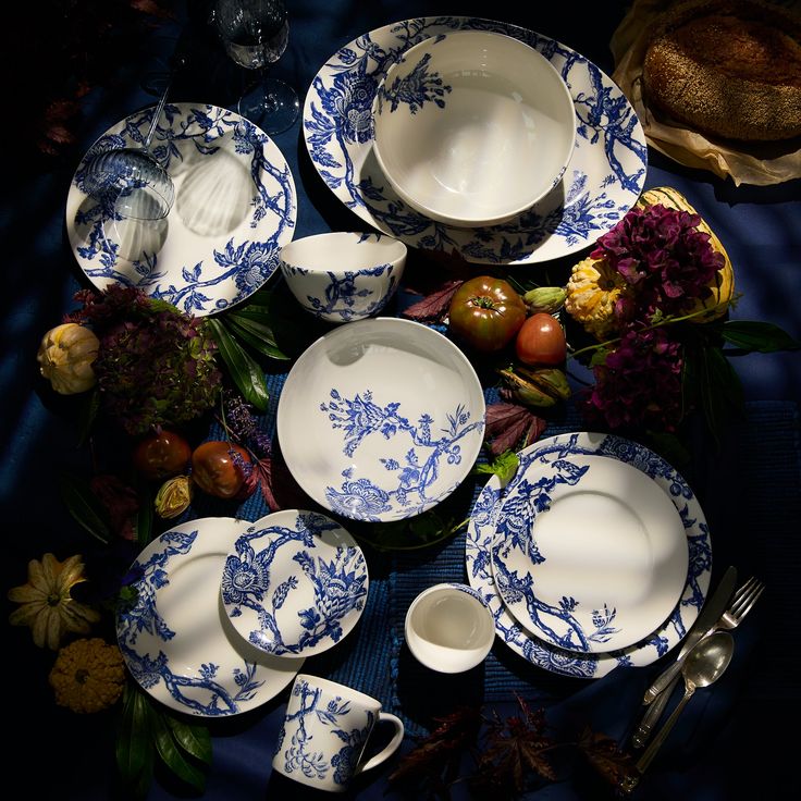 a blue and white dinner set on a table with flowers in the center, next to other dishes