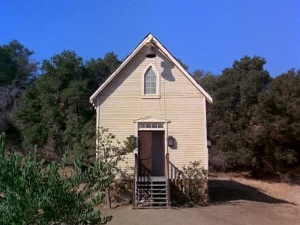 a small white building with a door and steps leading up to the front entrance is surrounded by trees