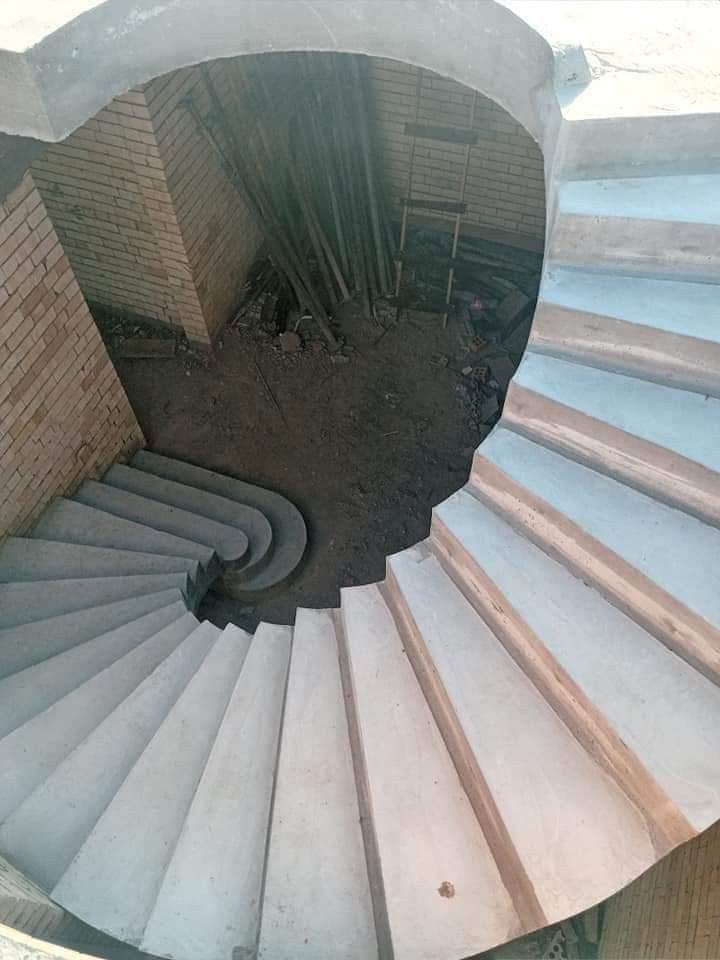 an aerial view of a spiral staircase made of concrete blocks and wood planks, with dirt on the ground below