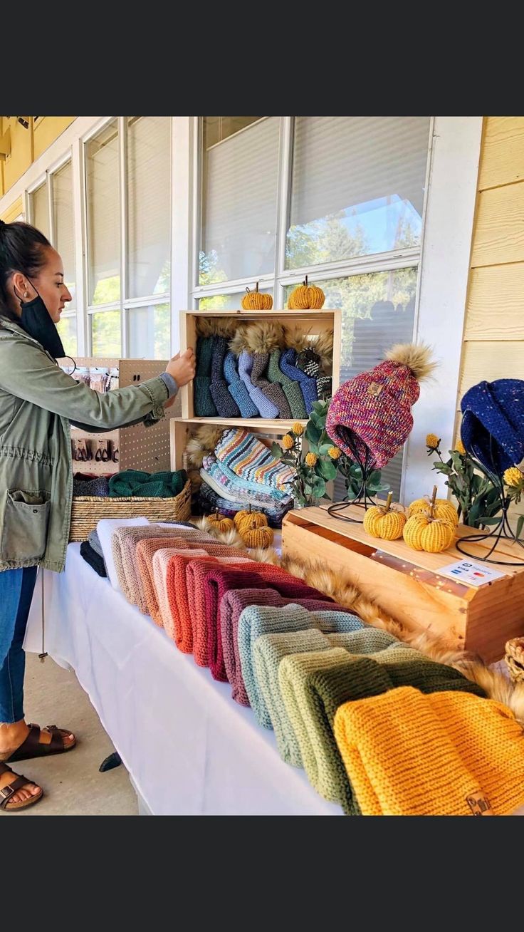 a woman standing in front of a table filled with knitted items