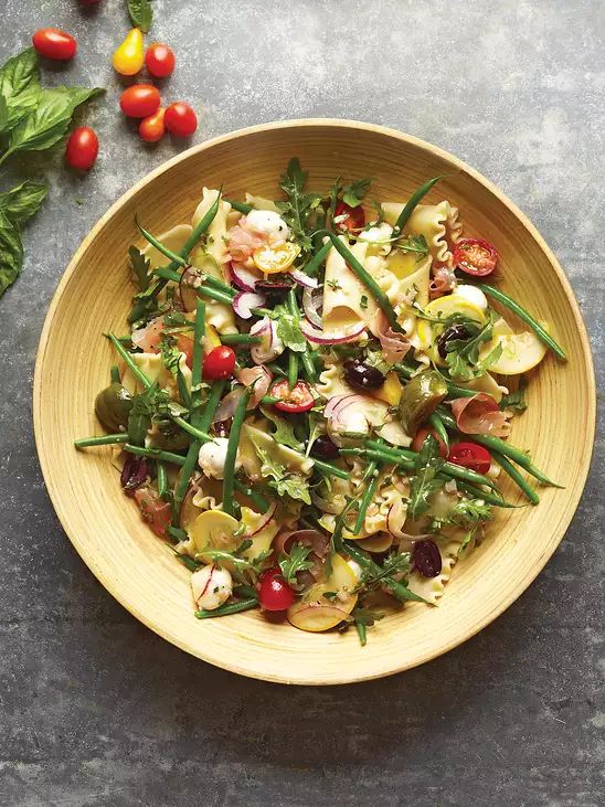 a yellow bowl filled with pasta and veggies on top of a gray table