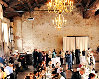 a large group of people standing around tables in a room with chandeliers hanging from the ceiling