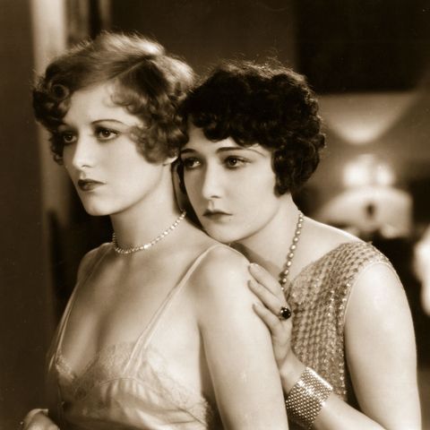 two women in evening dresses standing next to each other with pearls on their necklaces