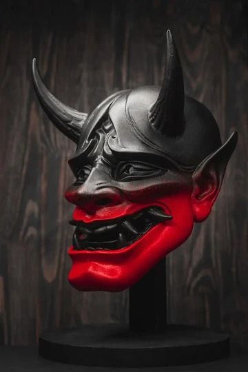 a red and black mask with horns on it's head is sitting in front of a wooden wall