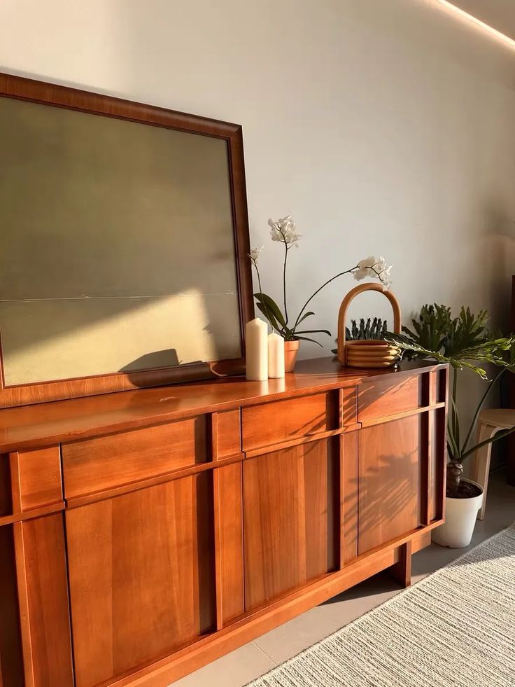 a large wooden dresser sitting next to a plant in a vase on top of a rug