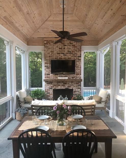 a covered patio with table, chairs and television on the wall in front of an outdoor fireplace