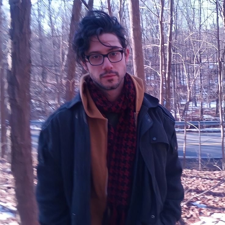 a man standing in the woods wearing glasses