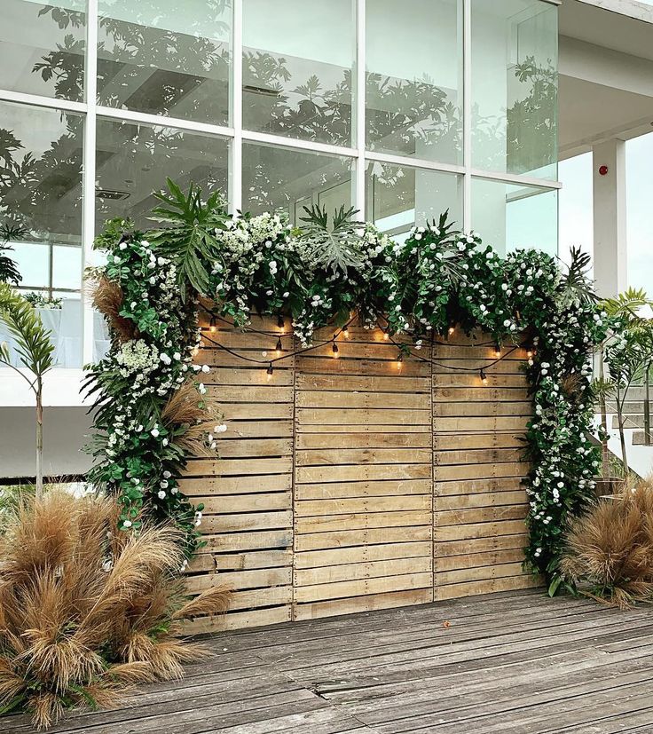 an outdoor wedding setup with greenery and lights in front of a large glass window