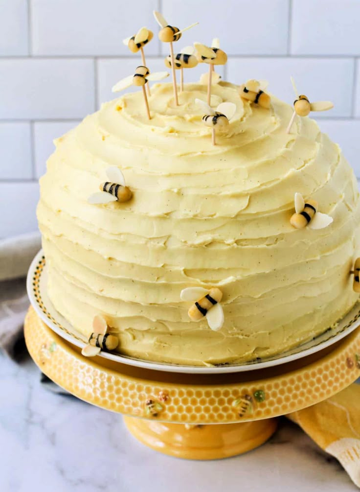 a yellow cake with white frosting and bees on top is sitting on a platter