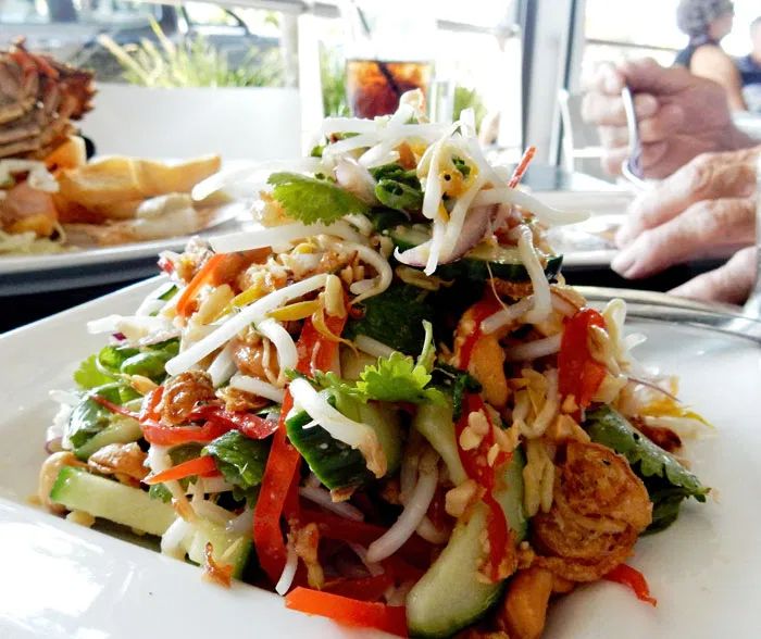 a white plate topped with salad next to another plate filled with food on top of a table