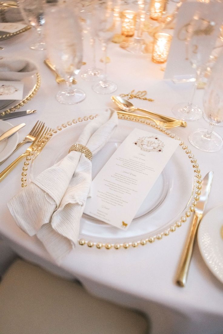 a table set with white and gold place settings, silverware, and napkins