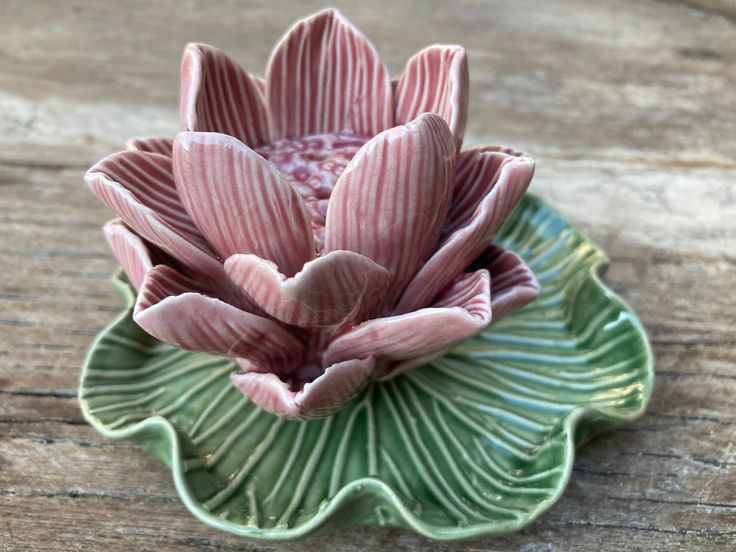 a small ceramic flower sitting on top of a green leafy dish with pink and white stripes