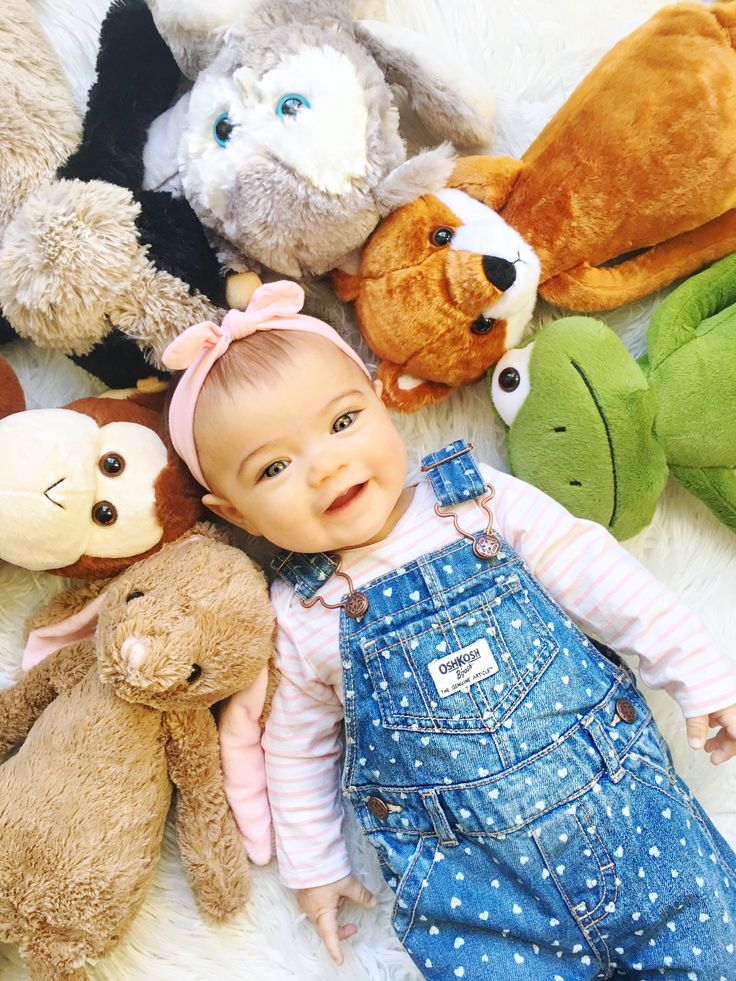 a baby laying on top of a pile of stuffed animals next to other stuffed animals