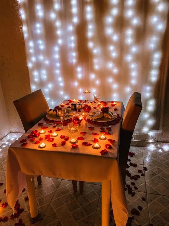 a dining room table set with candles and rose petals on the table for a valentine's day dinner