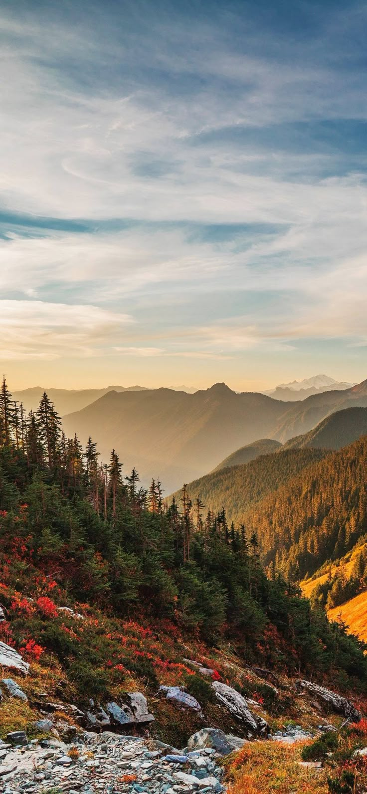 the mountains are covered in trees and rocks as the sun is setting on top of them