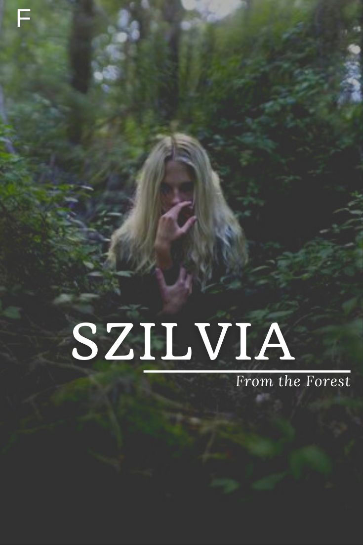 a woman is standing in the woods with her hand up to her face and looking into the camera