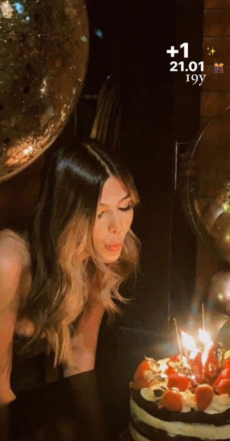 a woman sitting in front of a cake with lit candles on it and looking at the candle