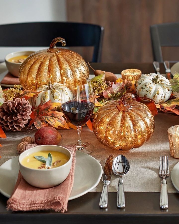 a table topped with plates and bowls filled with food next to silverware, candles and pumpkins