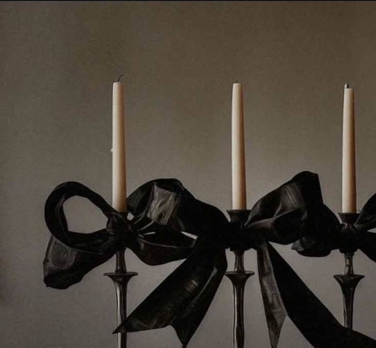 four candles with black bows on them are sitting in front of a wall and one candle is lit