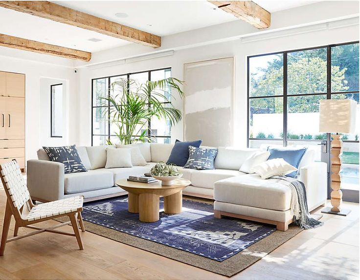 a living room with white couches and blue pillows on the rug in front of large windows