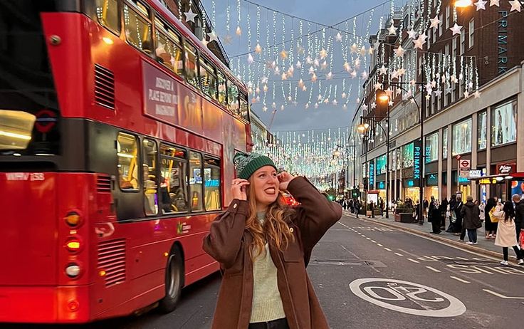 a woman standing on the side of a street next to a red double decker bus