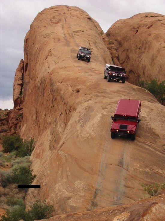 three trucks are driving on the side of a large rock formation in the middle of nowhere