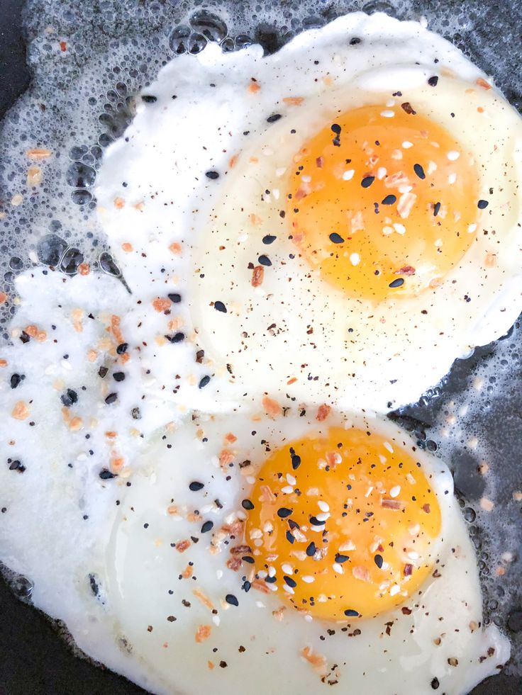 two fried eggs in a frying pan with black pepper sprinkled on them