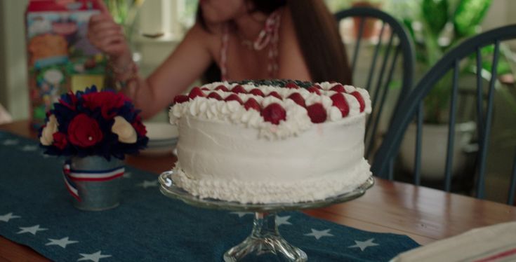 a woman sitting at a table in front of a cake with red, white and blue icing