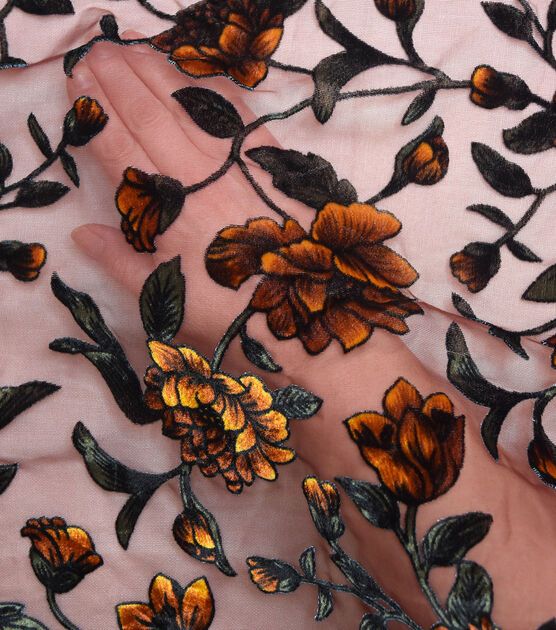 a woman's hand with an orange and black floral design on pink sheer fabric