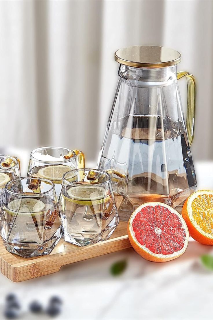 a wooden cutting board topped with sliced grapefruits and glasses next to a tea pot