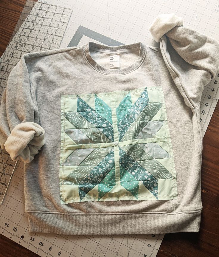 a sweatshirt with a quilted design on it sitting on top of a cutting board