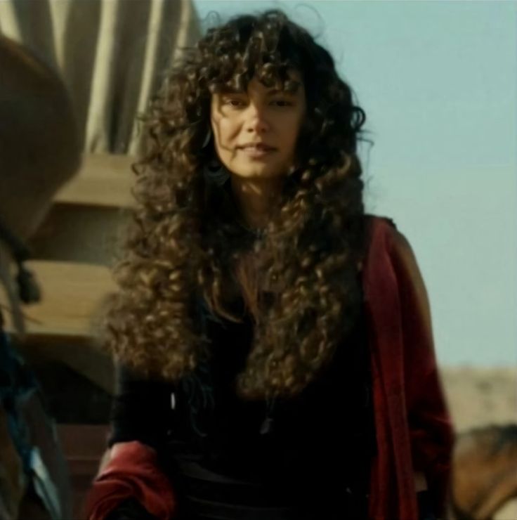 a woman with long curly hair standing next to a horse