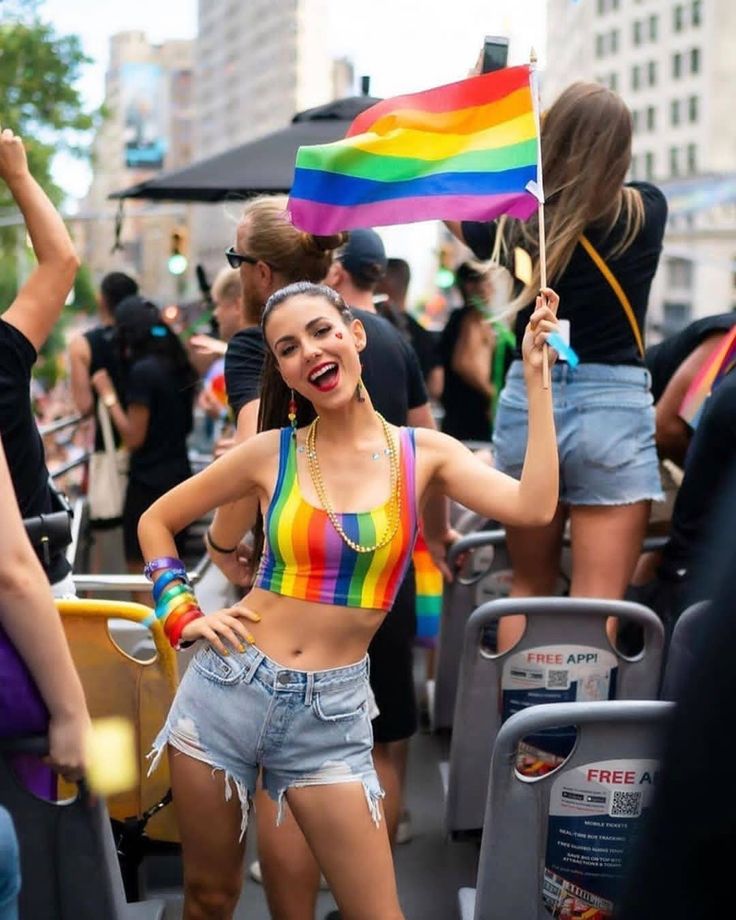 a woman is holding a rainbow flag in the middle of a crowded street with other people