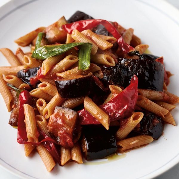 pasta with eggplant, olives and peppers on a white plate sitting on a table