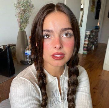 a woman with long braids sitting in front of a table and looking at the camera