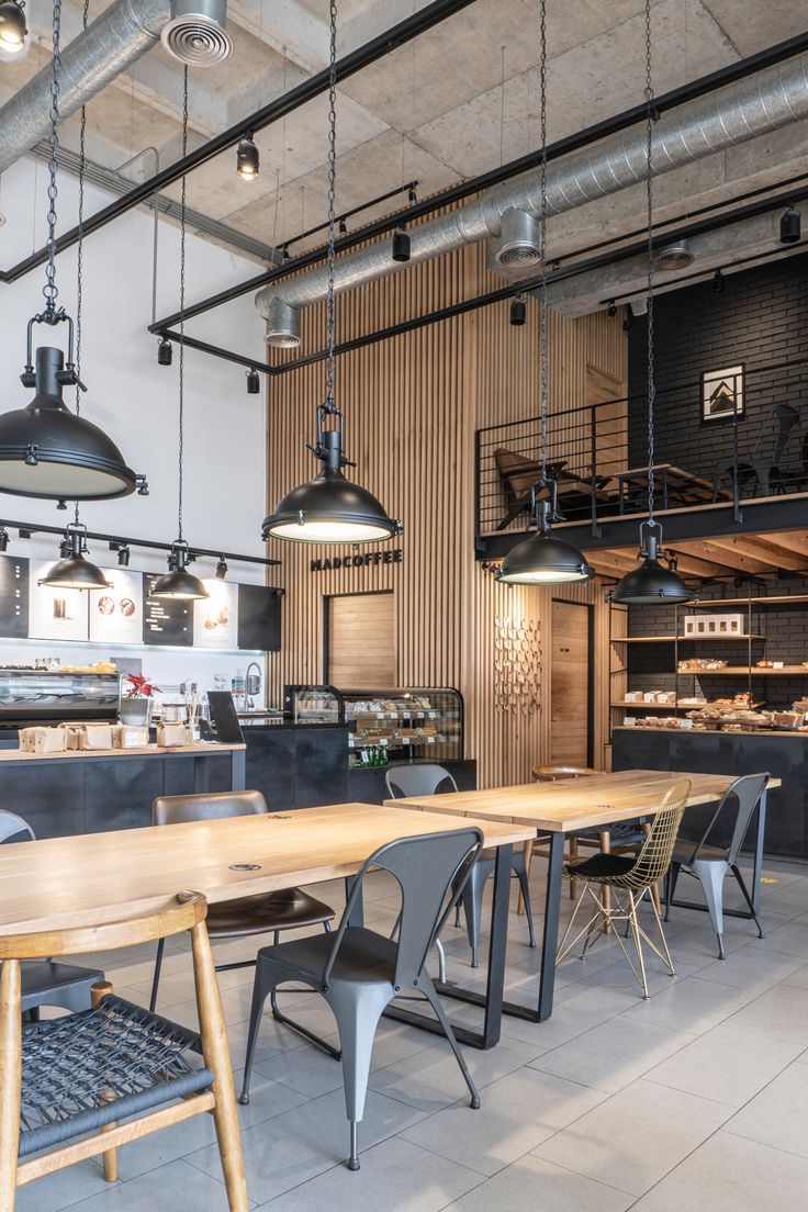 an industrial style restaurant with wooden tables and hanging lights over the kitchen counter, along with black chairs