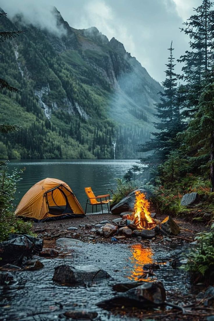 a tent is set up on the shore of a mountain lake next to a campfire