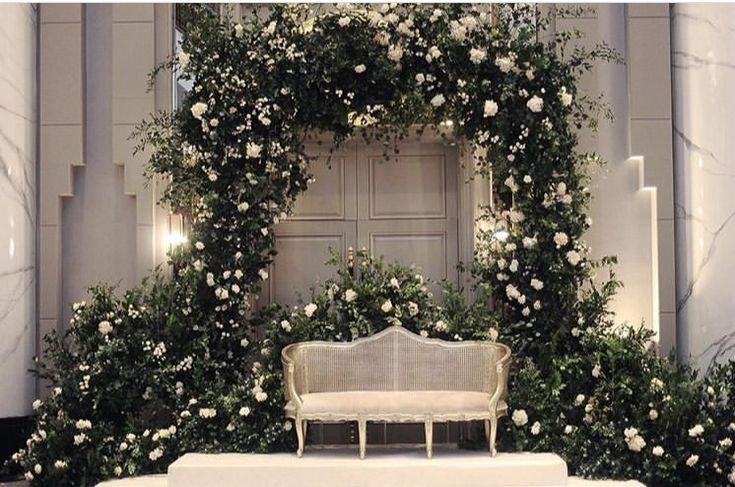 a white bench surrounded by flowers and greenery in front of a doorway with an arch