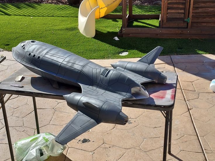 a model airplane sitting on top of a metal table next to a swing set in the back yard