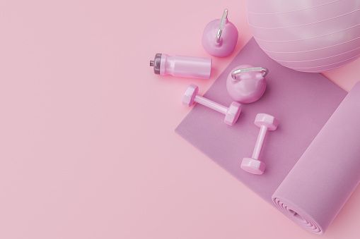 an exercise mat, dumbbells, and bottle of water on a pink background