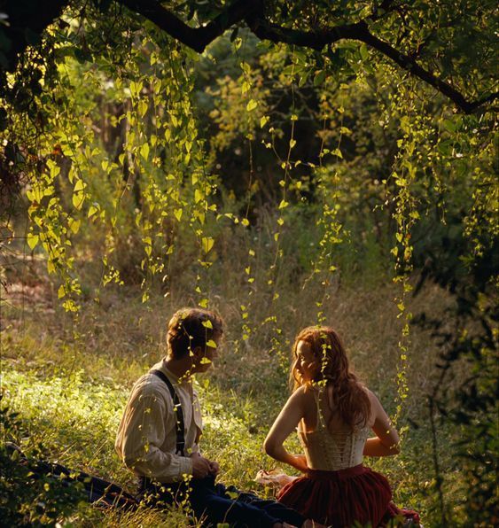 a man and woman sitting on the ground next to each other in front of trees