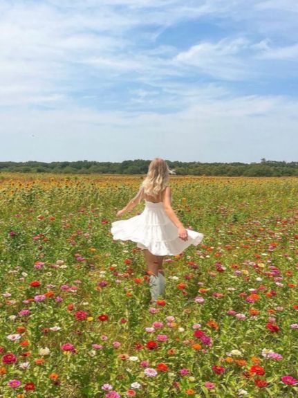 a woman in a white dress walking through a field full of flowers