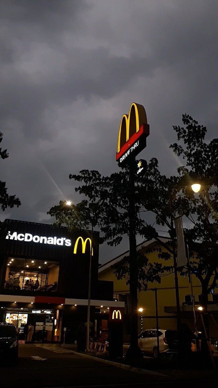 a mcdonald's restaurant is lit up at night with dark clouds in the background