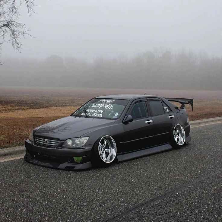 a black car parked on the side of a road in front of a foggy field