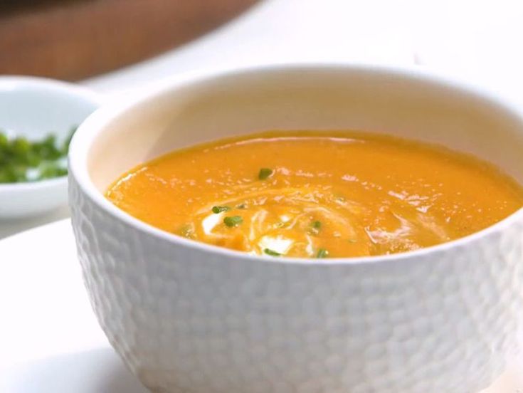 a white bowl filled with carrot soup next to a small bowl of green garnish