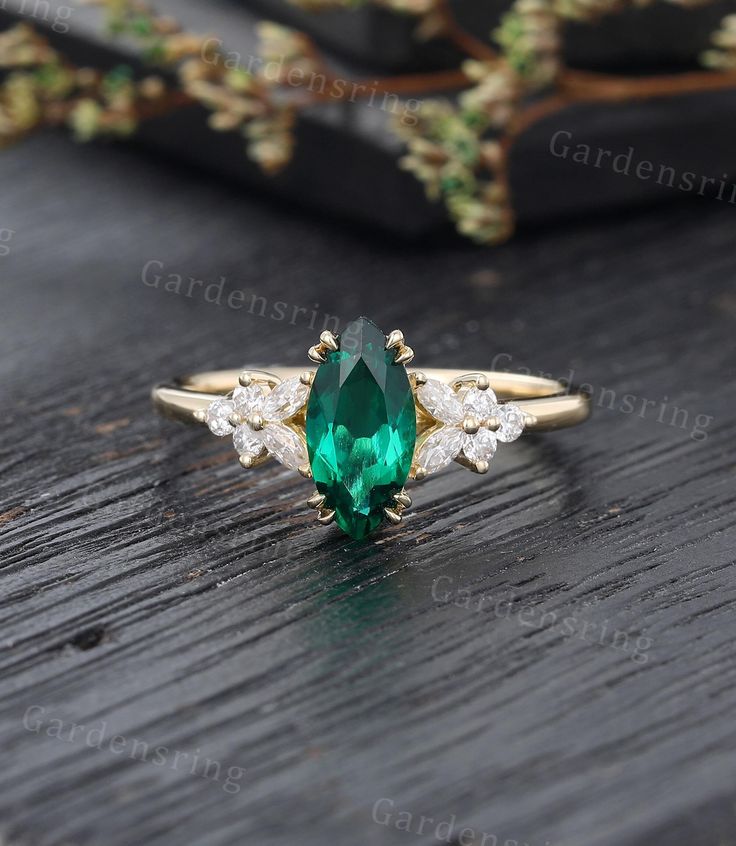 an emerald and diamond ring sitting on top of a wooden table next to a potted plant