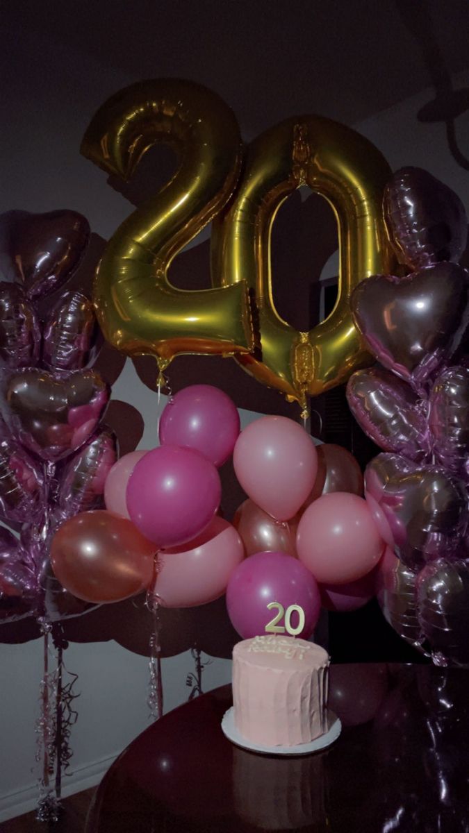 a table topped with balloons and a cake covered in pink frosting next to a number twenty sign