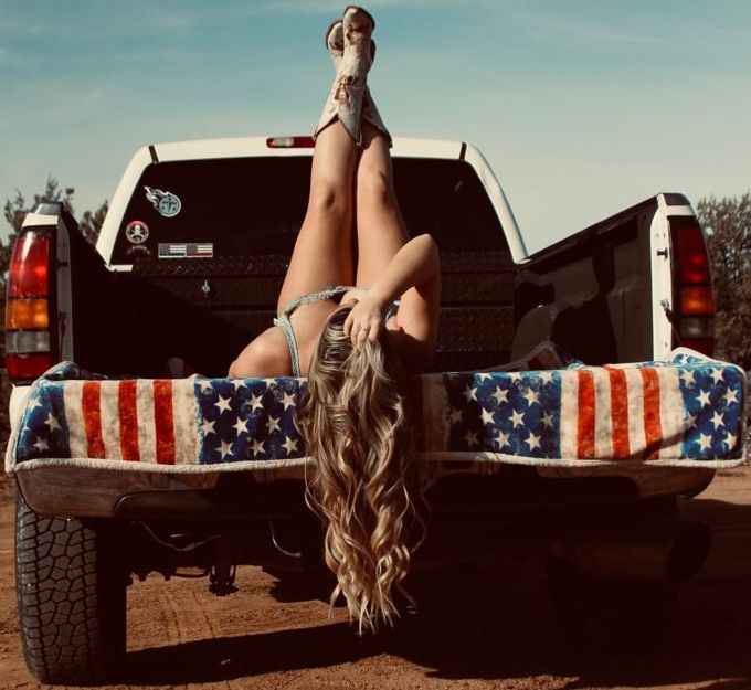 a woman laying on the back of a truck with an american flag blanket draped over it